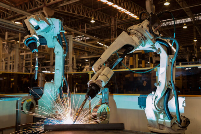 Two robotic manufacturing machines welding a metal part