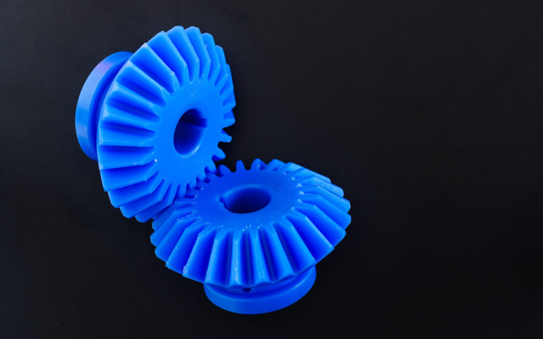 Two blue bevel gears made from plastic, placed together to create a miter gear